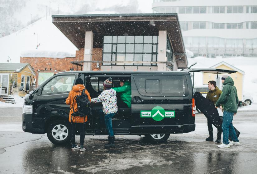 A black van being loaded with passengers and ski gear