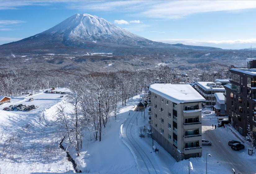 A snow covered landscape with Mount Yotei behind and hotel building to the right