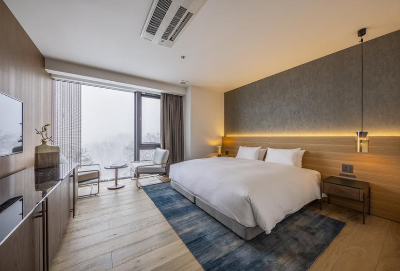 A made up double bed with pendant light to the right