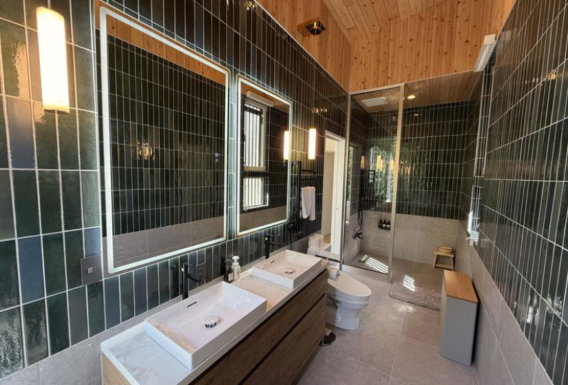A green tiled bathroom with two mirrors and shower behind