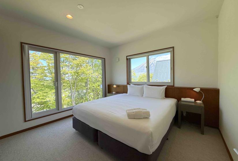 A made up double bed with windows to the left