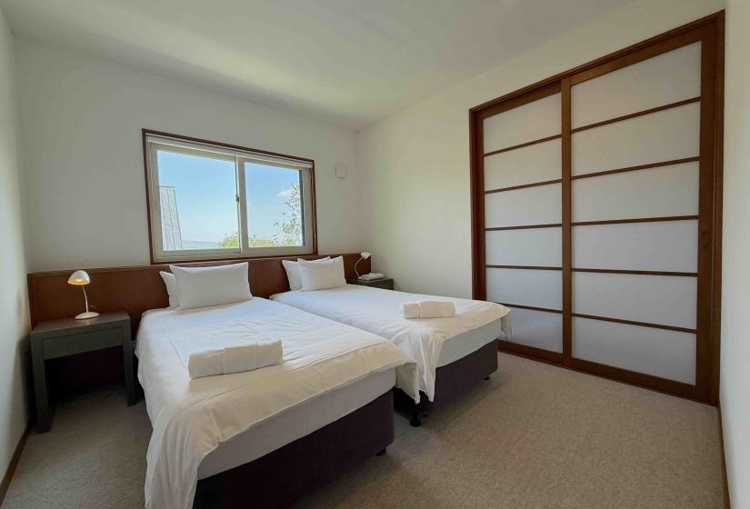 Two made up single beds together with towels at their foot.
