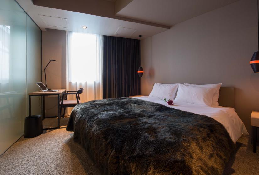 A made up double bed with dark throw
