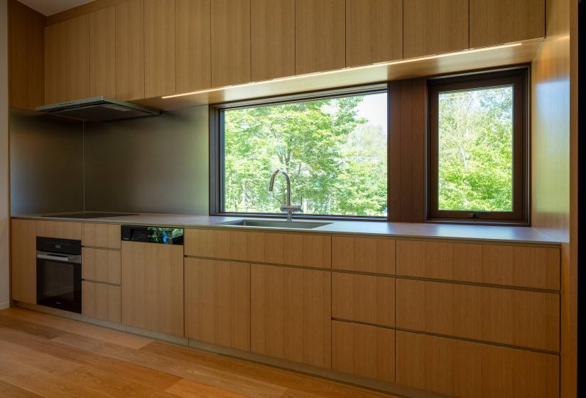 Setsuei Niseko kitchen with oak cabinetry and a window onto summer trees